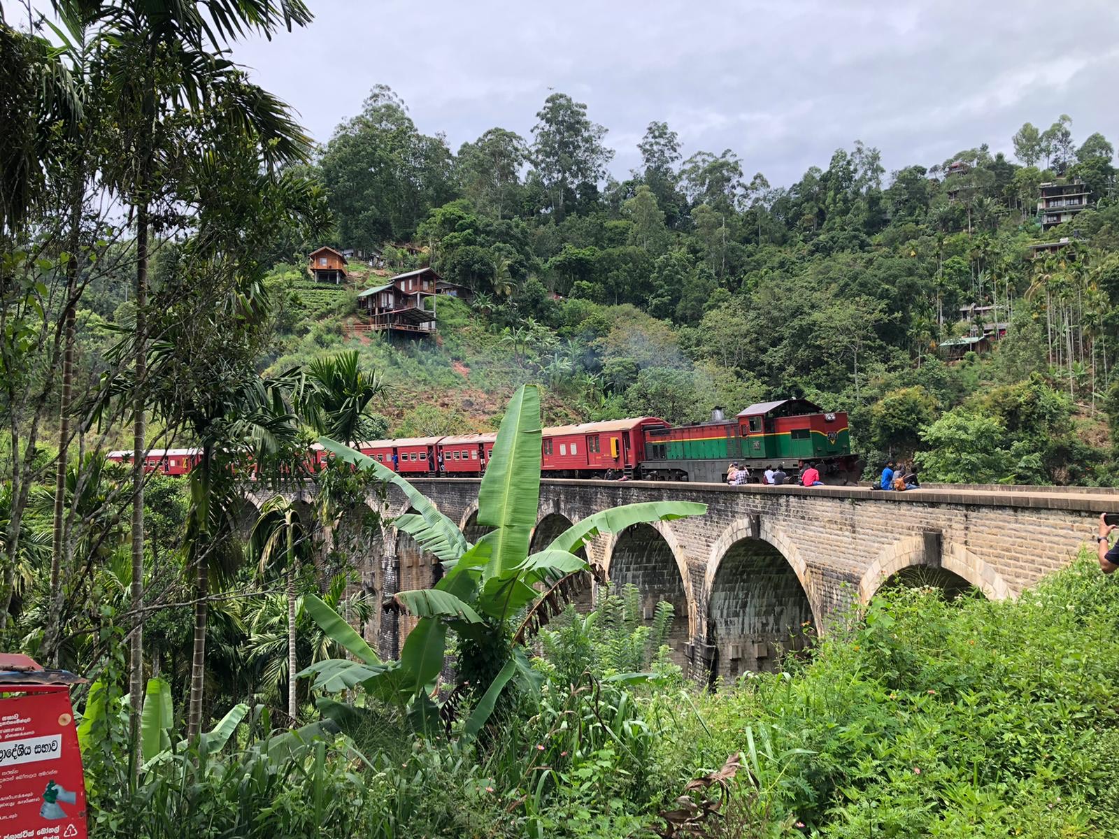 A train passes over a stone viaduct with local residents sitting on it